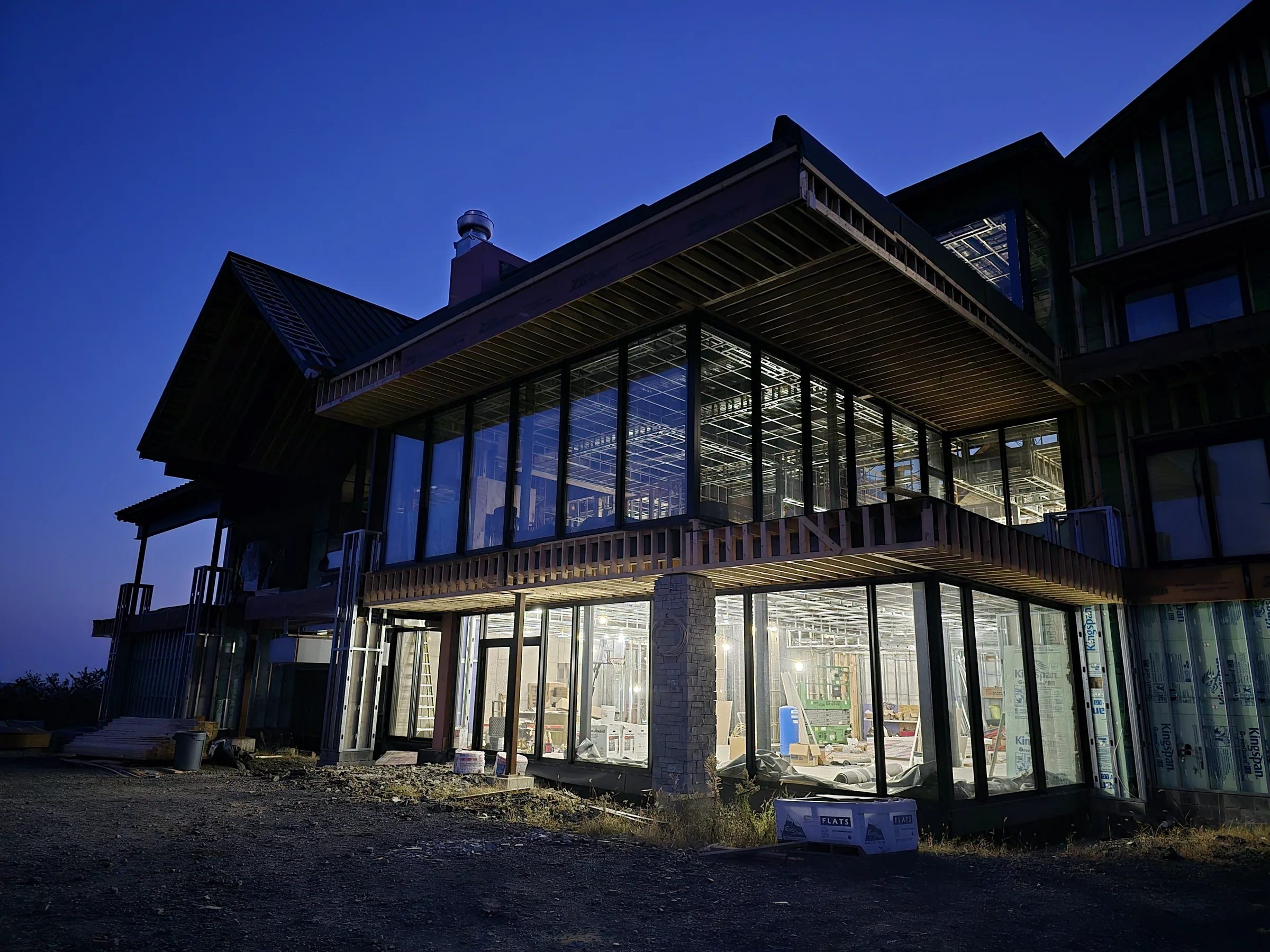 Stone, glazing, and rooflines of the Modern Mountain House at blue hour during construction