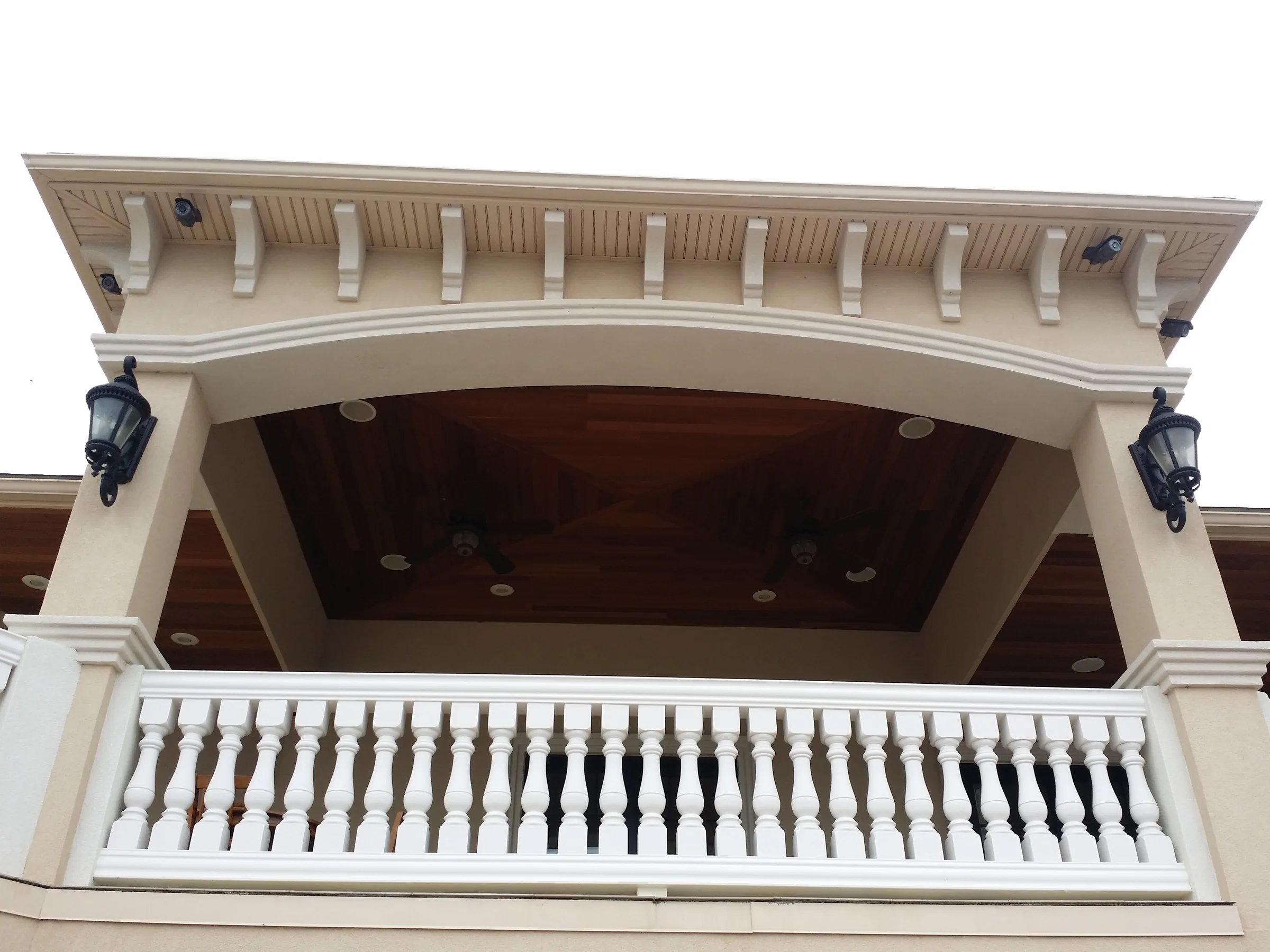 Detail of a covered balcony with bracketed wood soffit, an arched stucco surround, and a cast stone balustrade