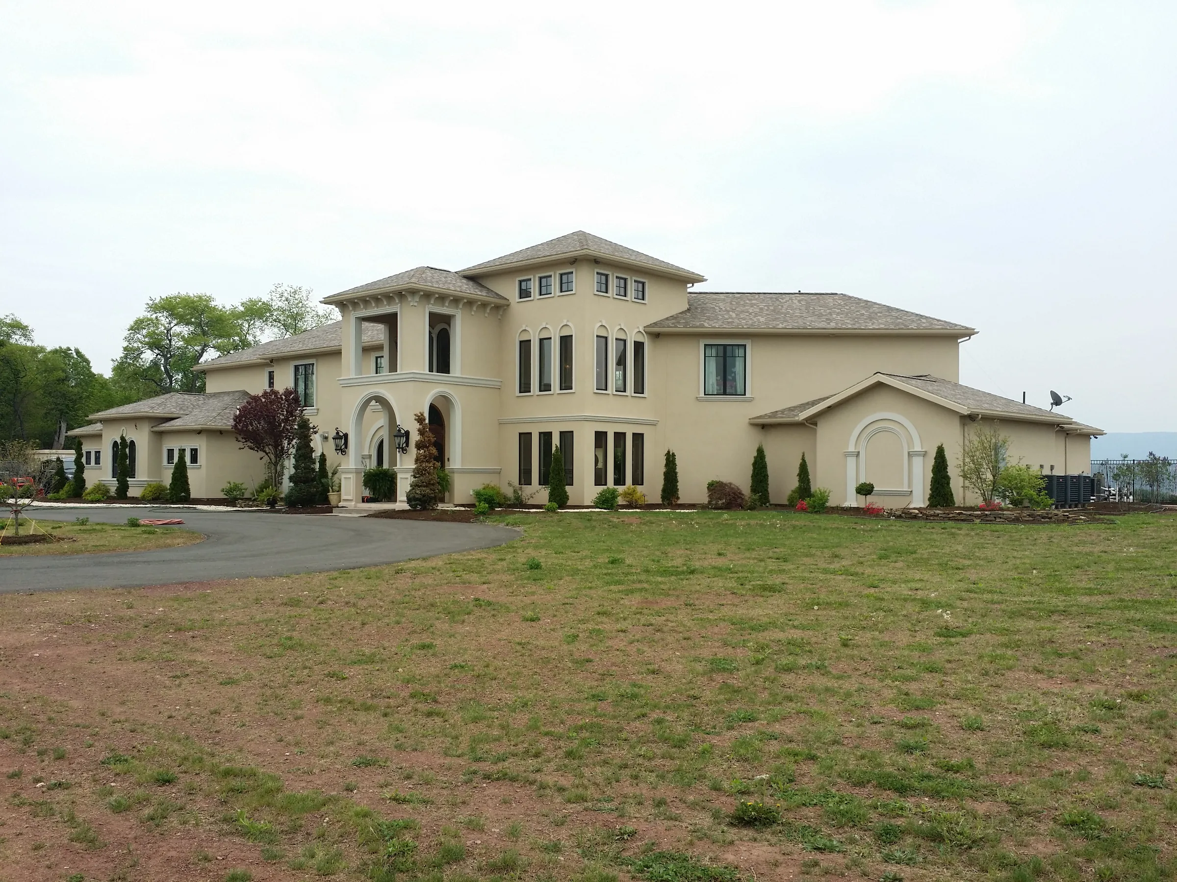 Two-story stucco villa with an arched entry loggia and landscaped grounds, seen from the front