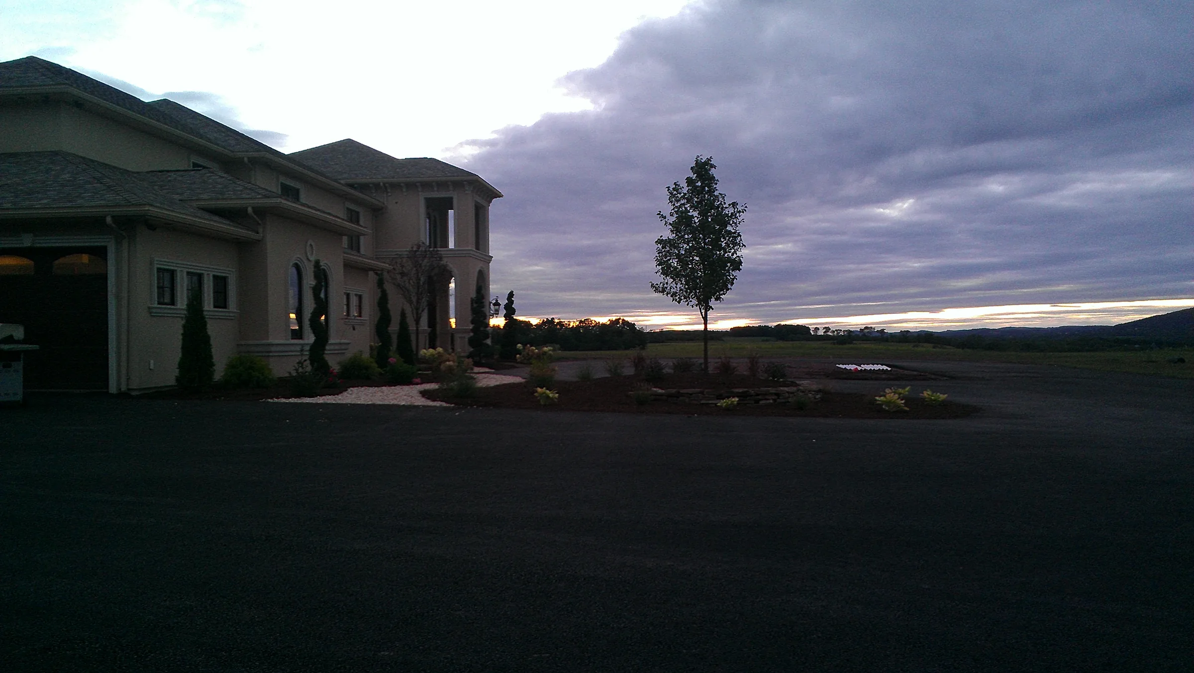 Completed stucco residence at dusk with a dramatic sunset sky and established landscaping