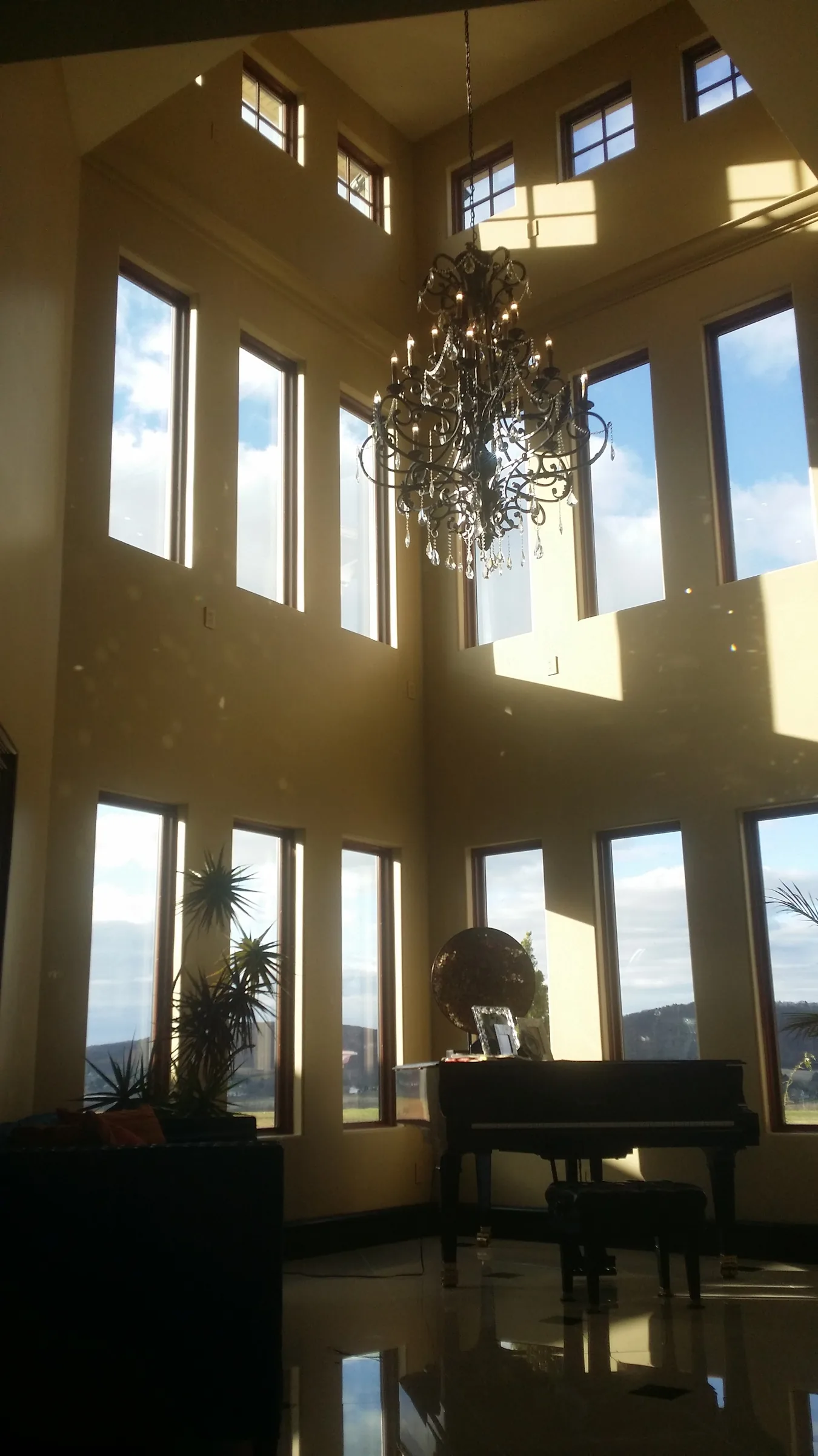 Two-story foyer corner with tall arched windows, a wrought-iron chandelier, and a grand piano
