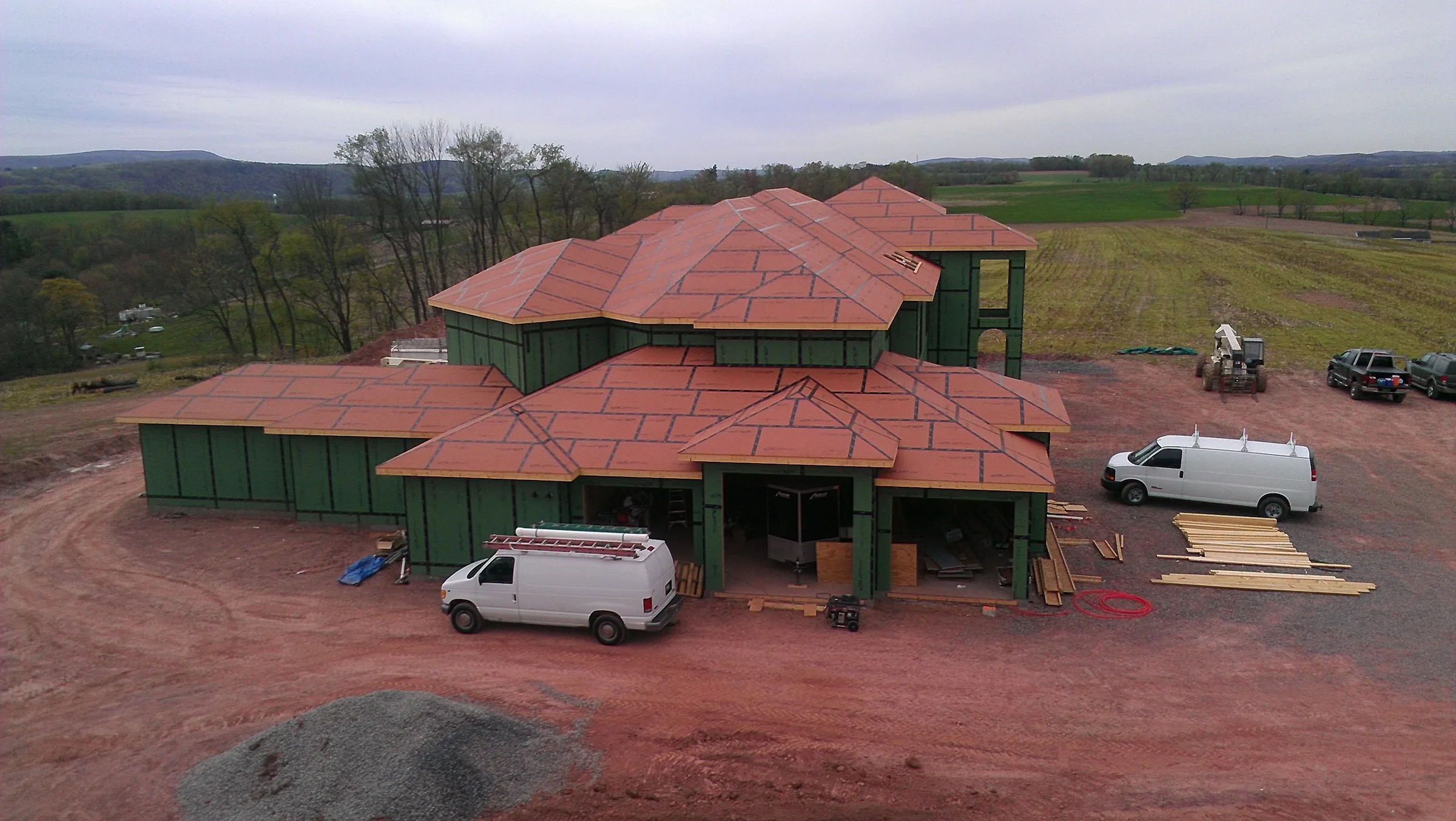 Elevated view of a large residence during construction, with roof sheathing complete and wall panels installed