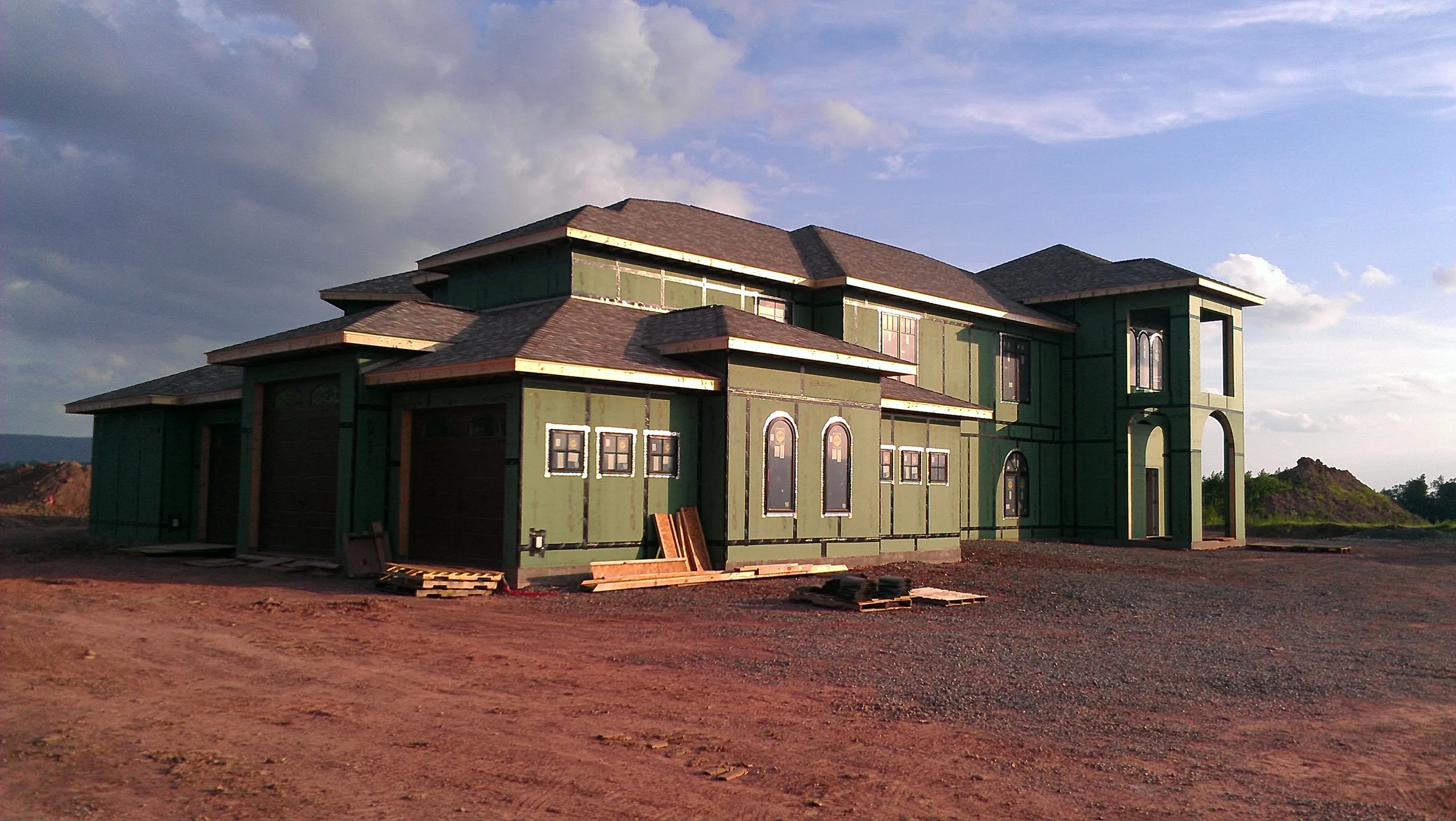 Ground-level view of the framed and sheathed residence shell under a dramatic sky before finishing