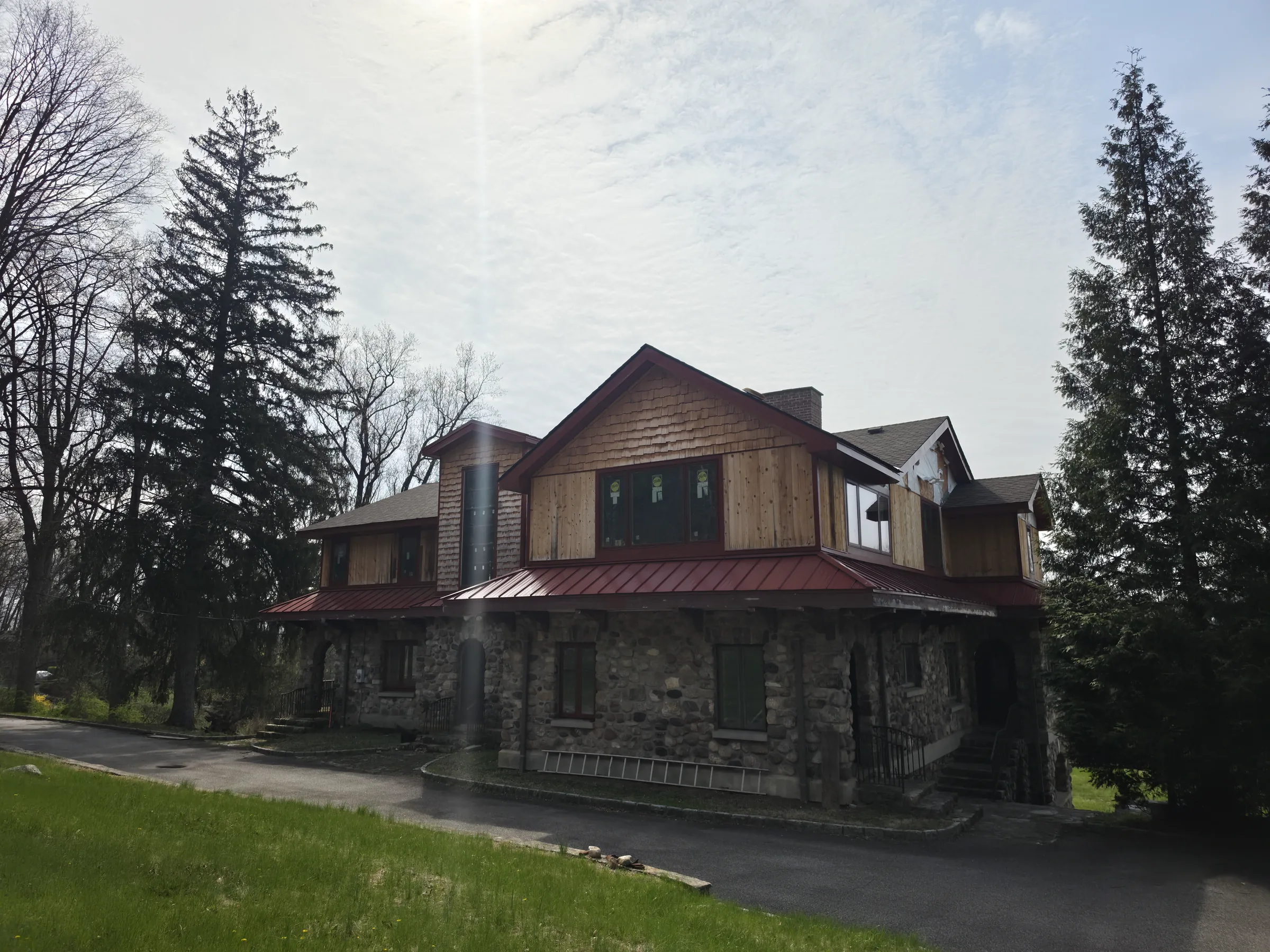 Closer view of the cedar-shingled front cross-gable and the stone chimney, with the red standing-seam roof running below