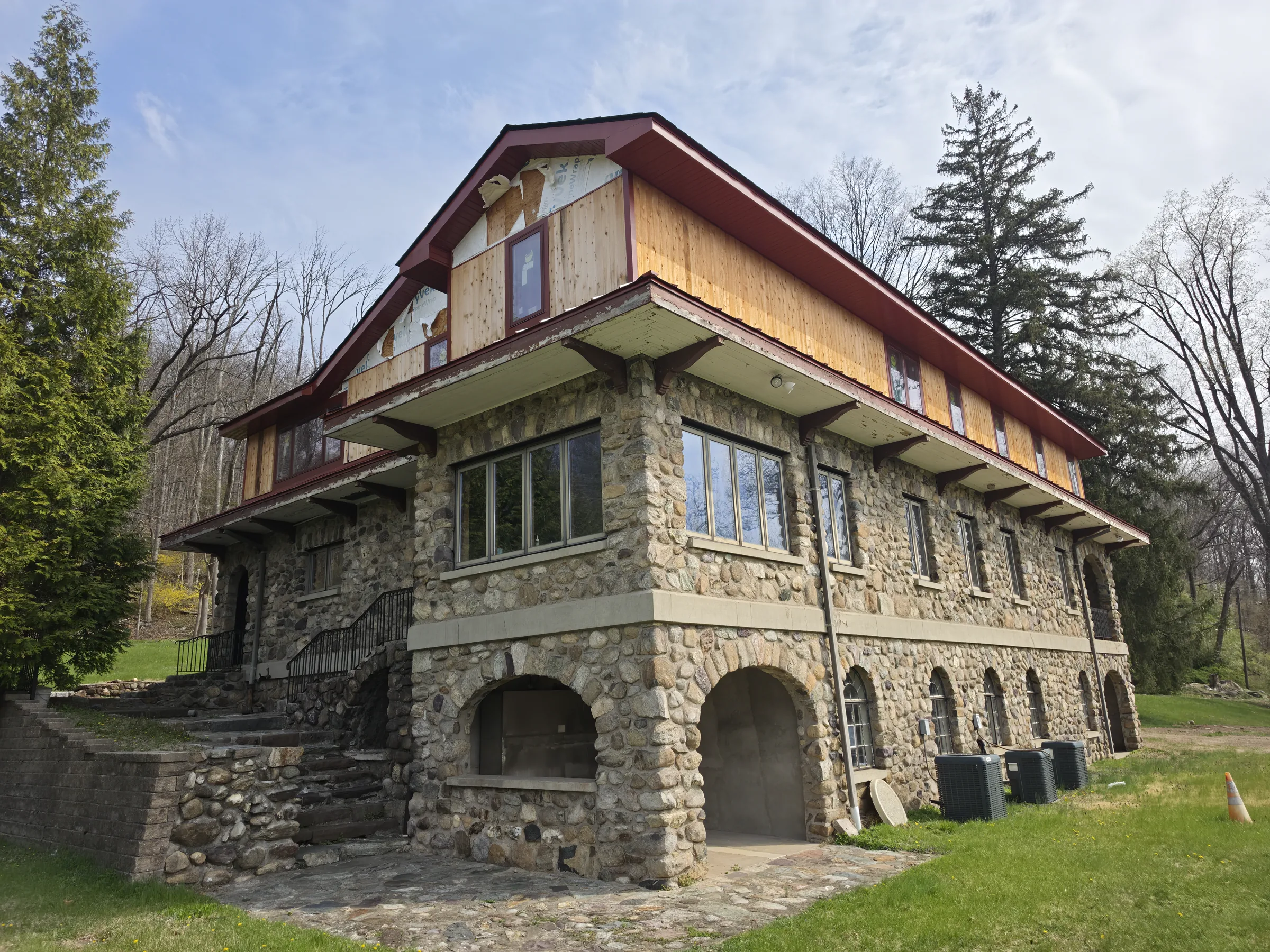 Ground-level view of the river-stone base showing arched recessed bays, a cast-stone band, and condenser units on the paved pad alongside